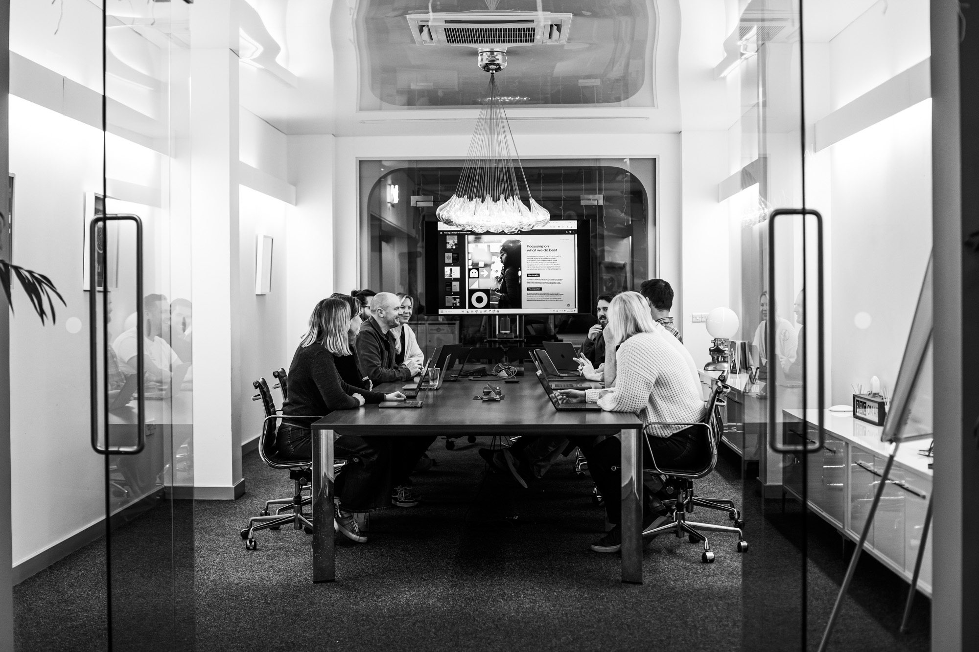 Business team meeting in modern glass conference room with laptops and presentation screen