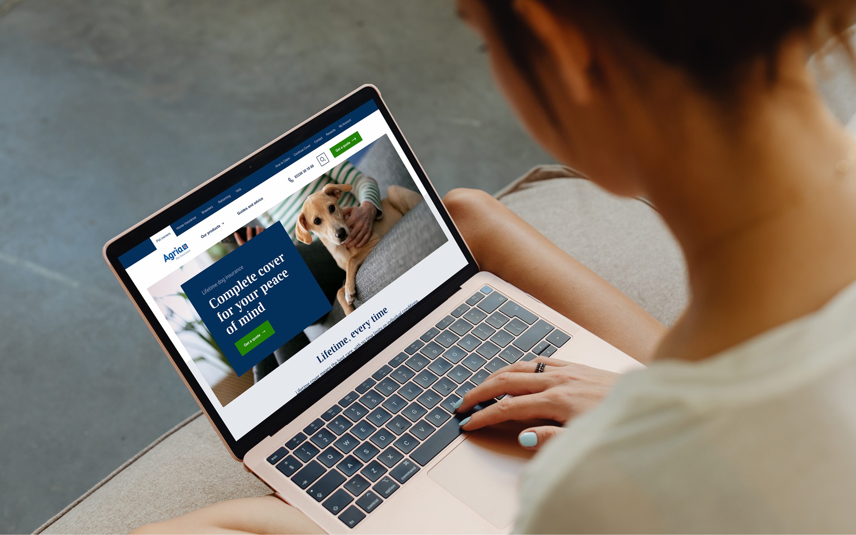 Woman using laptop displaying Agria pet insurance website with dog image and "Complete cover for your peace of mind" text