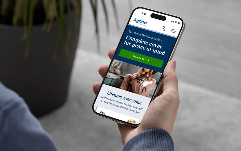 Hand holding smartphone displaying Agria pet insurance website with blue header and image of person holding cat