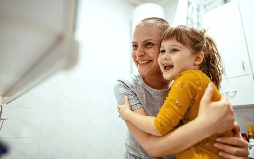 Smiling woman with short hair embracing young girl in yellow shirt in bright kitchen setting