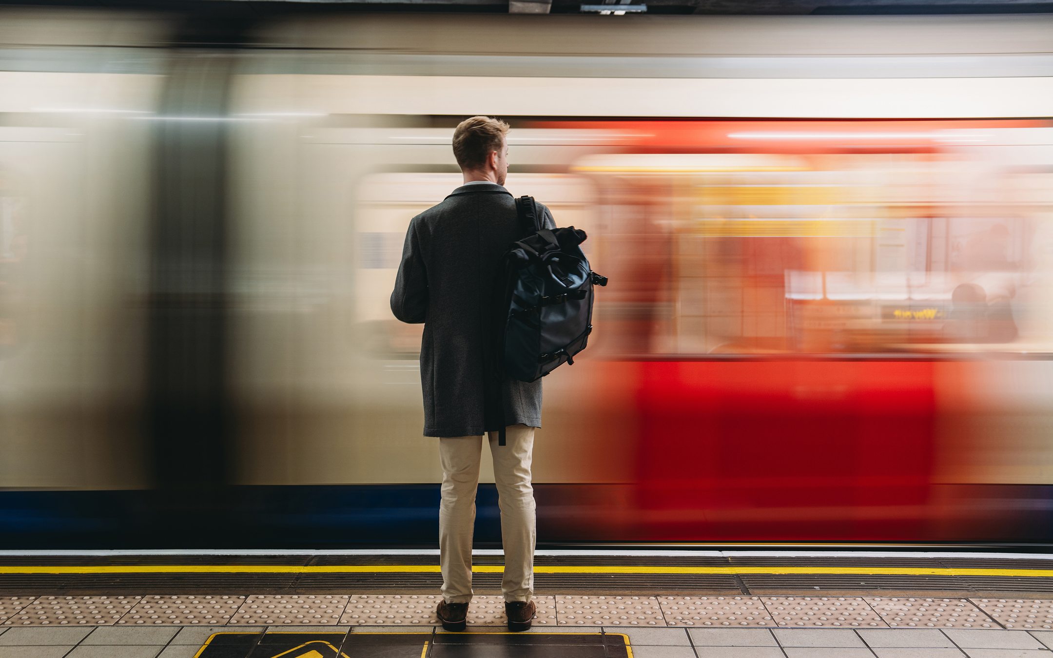 Man with backpack standing on subway platform as train passes by in motion blur