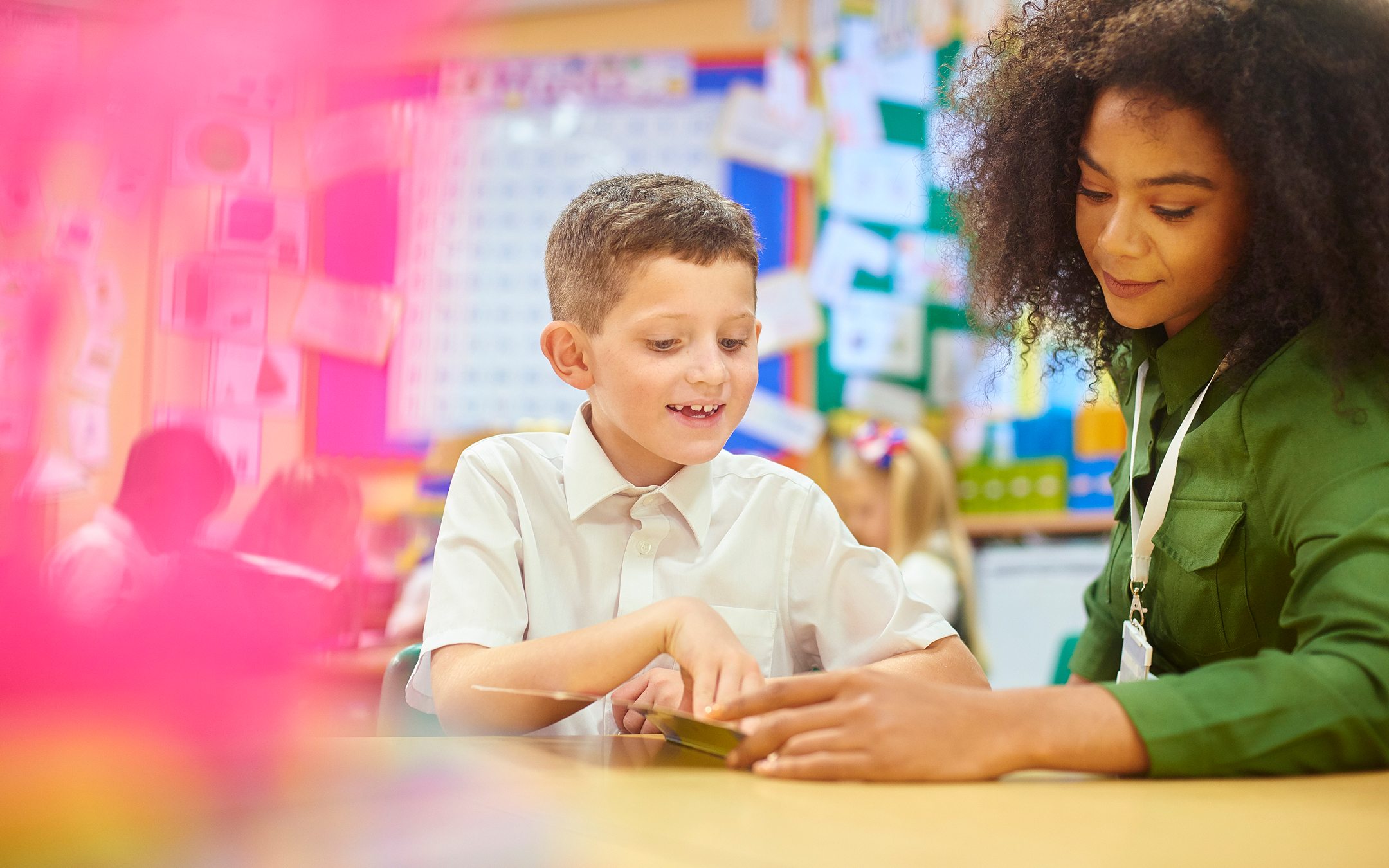 Teacher and young student working together with tablet in colorful classroom setting