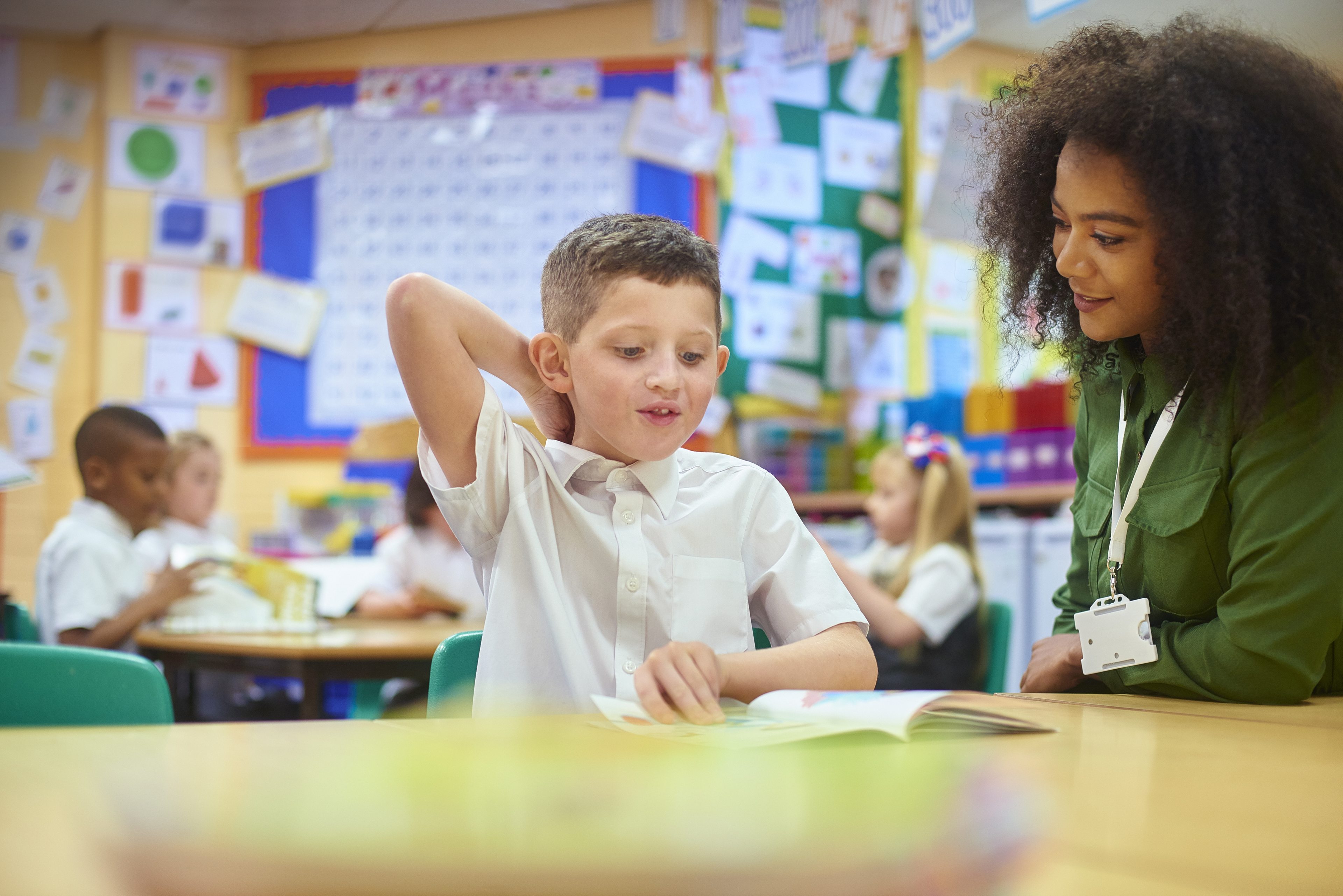 Teacher helping young student with schoolwork in colorful classroom setting