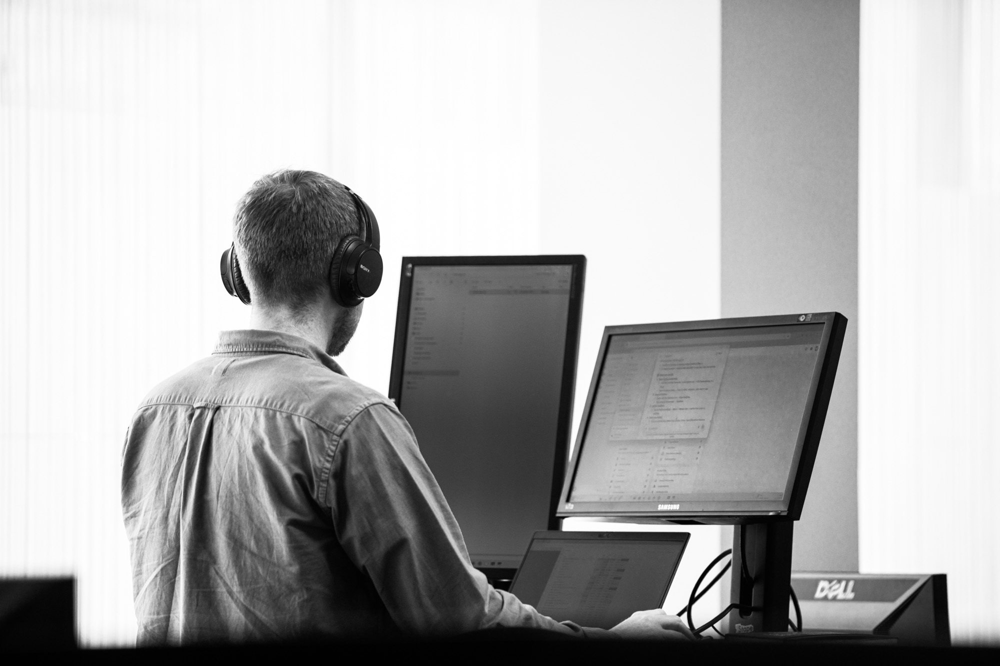 Person wearing headphones working at dual monitor computer setup in modern office workspace