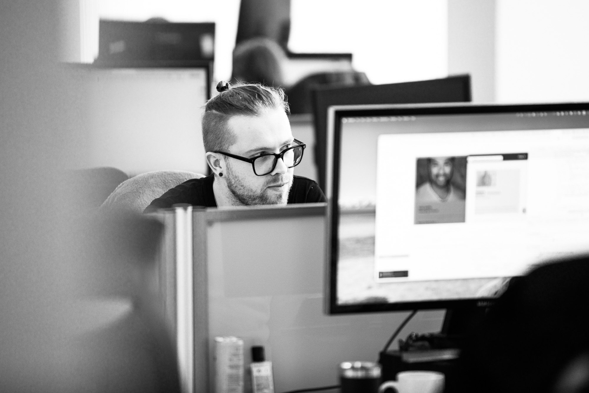 Man with glasses working at computer in modern office with multiple monitors