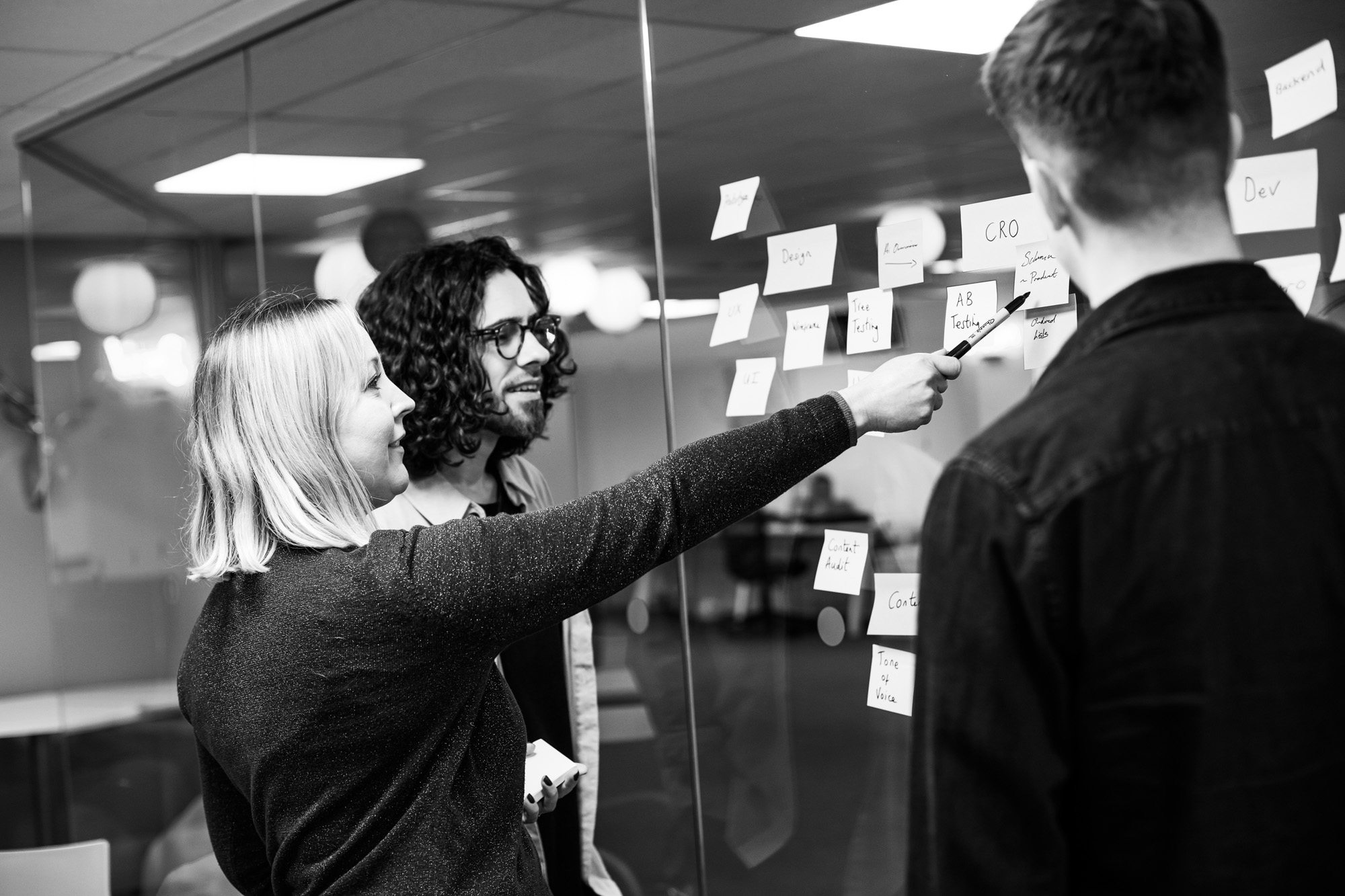 Three professionals collaborating at a glass wall with sticky notes in a modern office environment