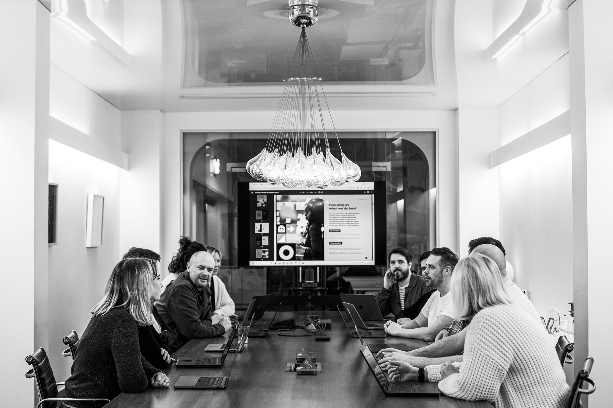 Business team meeting in modern conference room with laptops and presentation screen in black and white