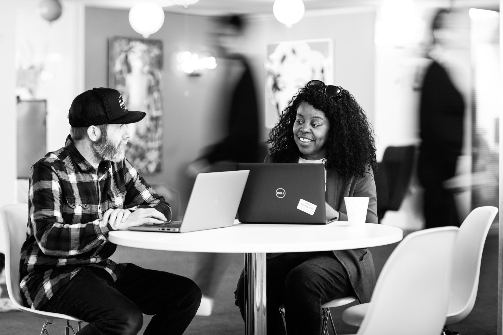 Two professionals collaborating at a table with laptops in a modern office space