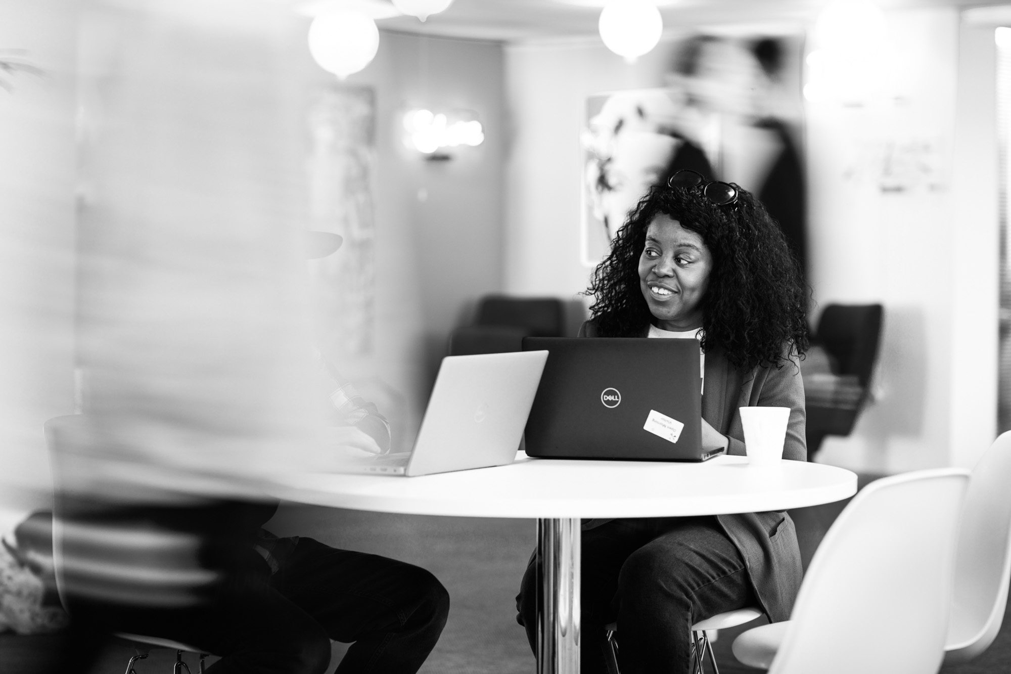 Woman with curly hair smiling while working on laptop at round table in modern office space