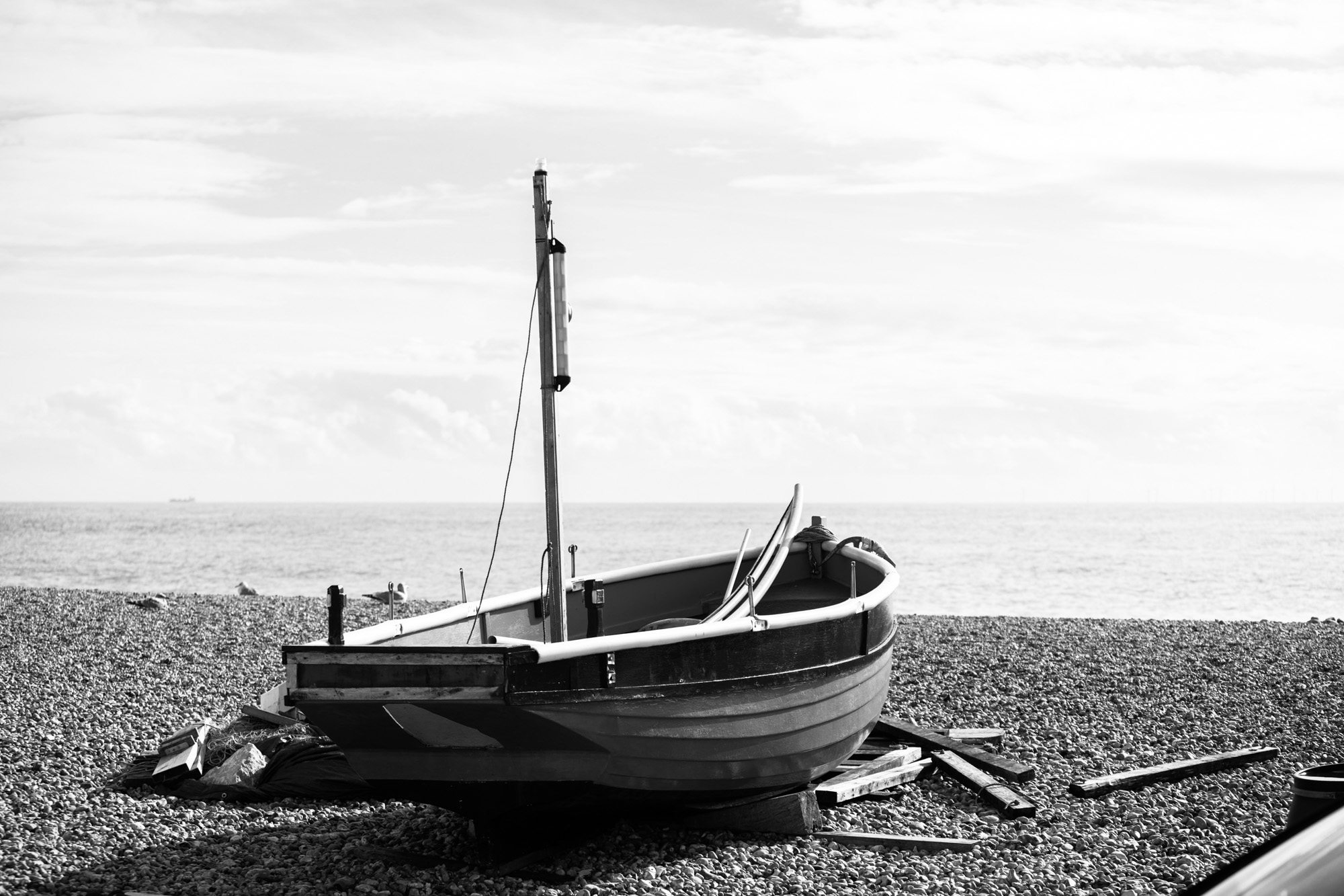 Black and white fishing boat beached on pebble shore with mast and rigging against cloudy sky