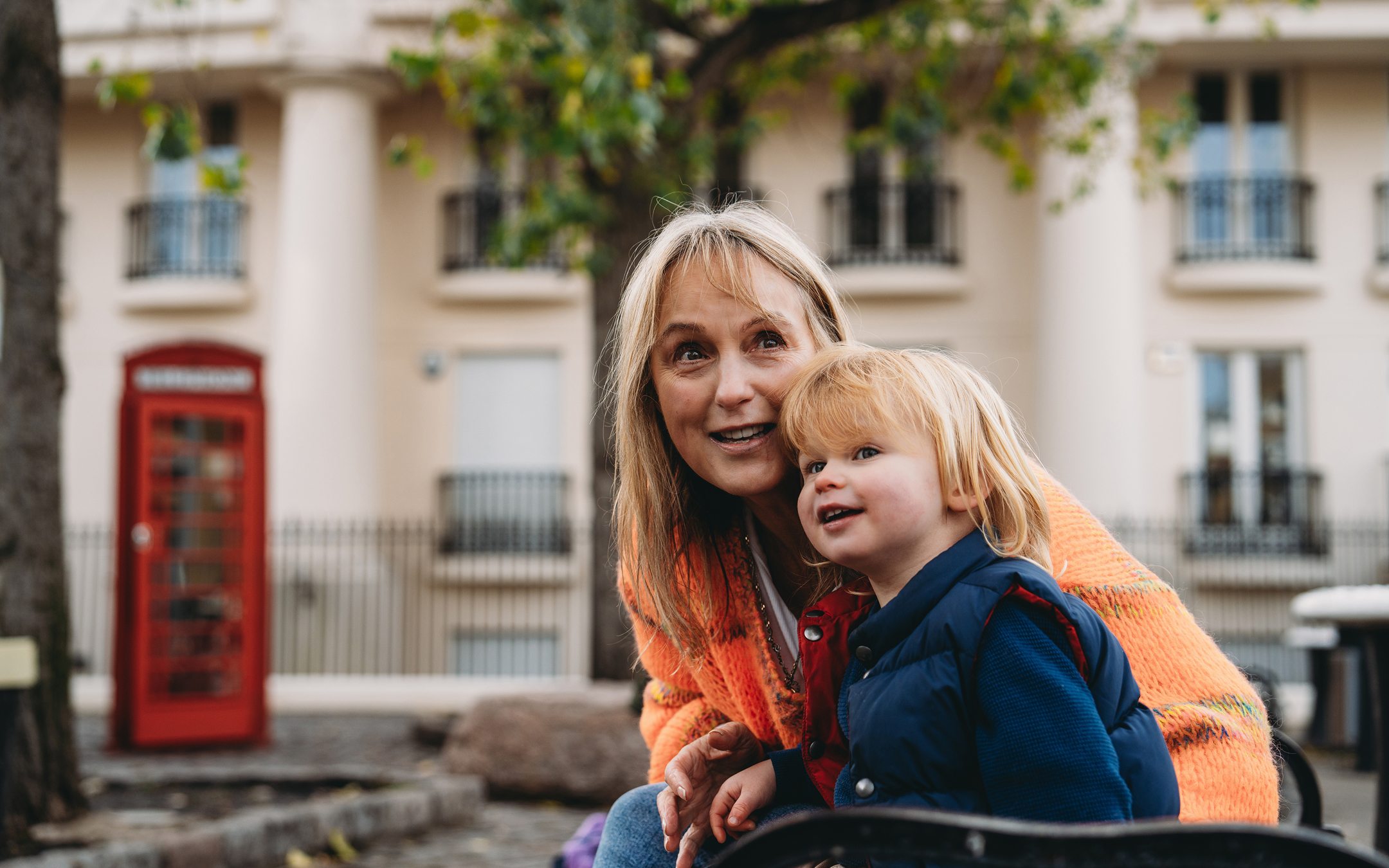 Woman and young child smiling outdoors in front of London street with red phone box and Georgian buildings