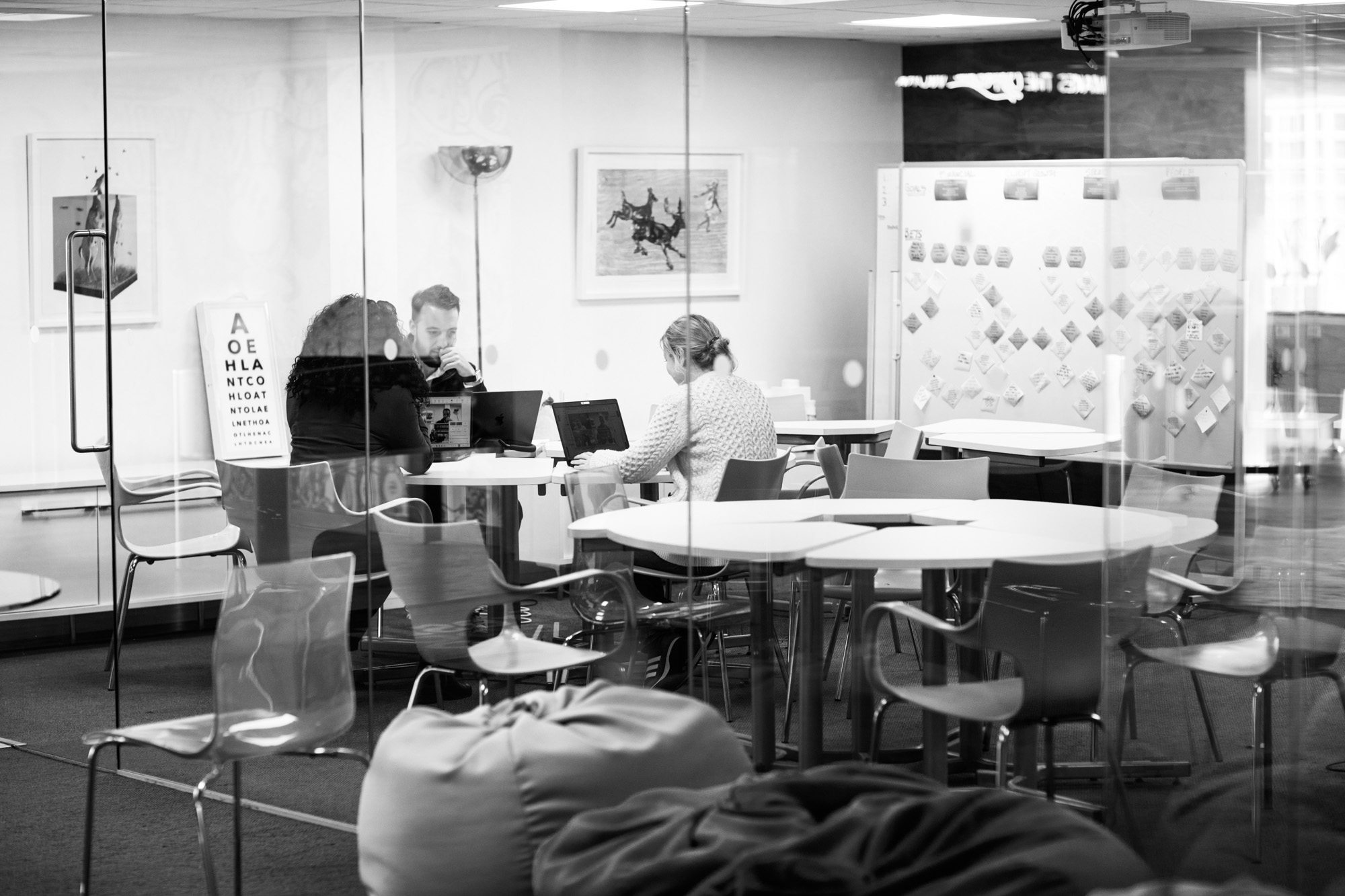 Three people working on laptops at modern white desks in a bright office space with glass walls and contemporary furniture