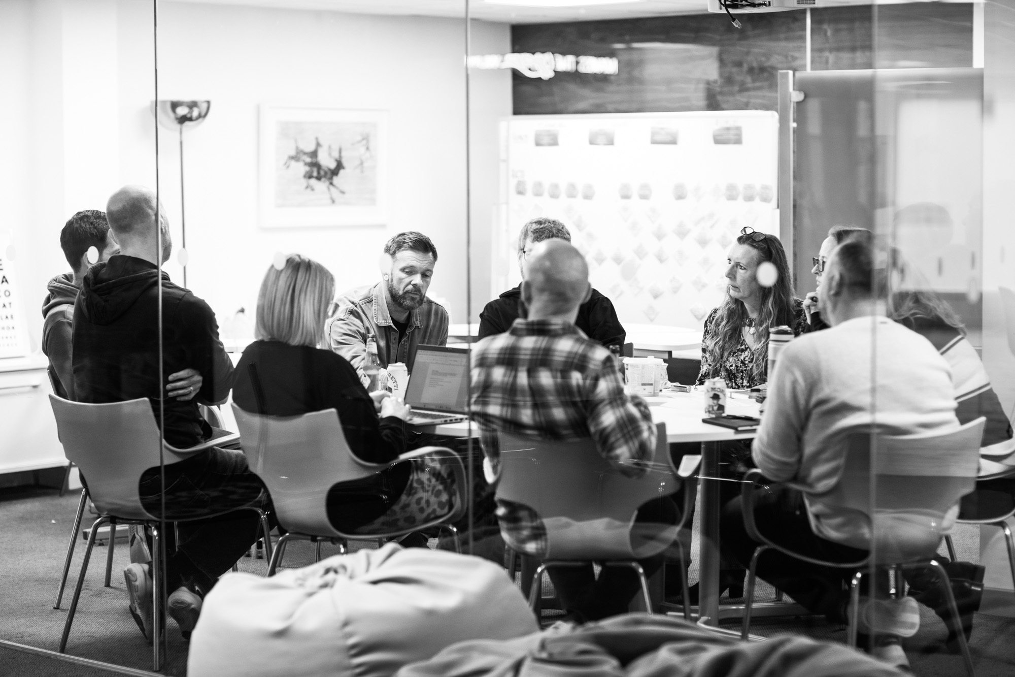 Team meeting in modern office with people sitting around table, some wearing headphones, black and white photo
