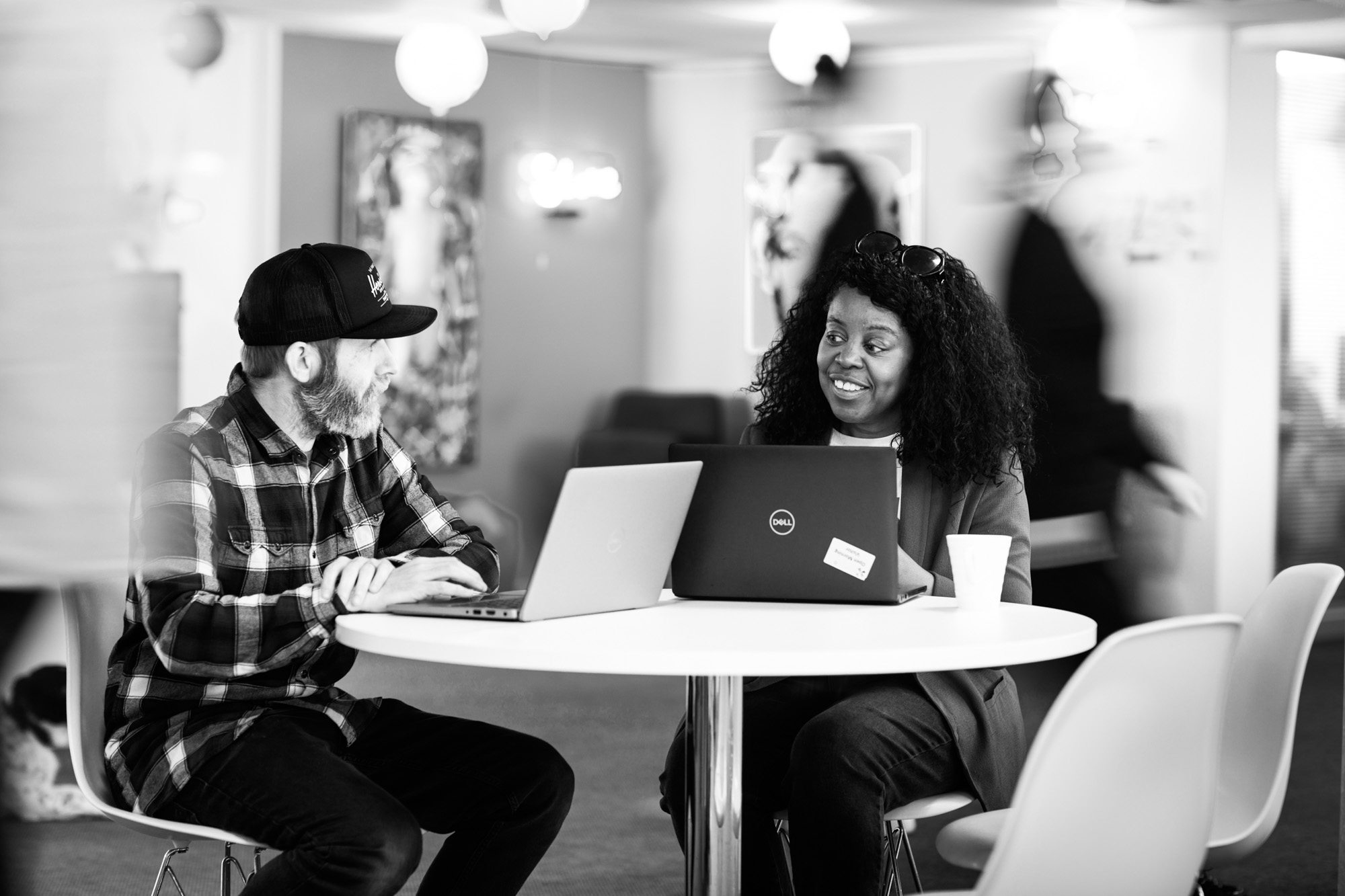 Two professionals collaborating at a table with laptops in a modern office space