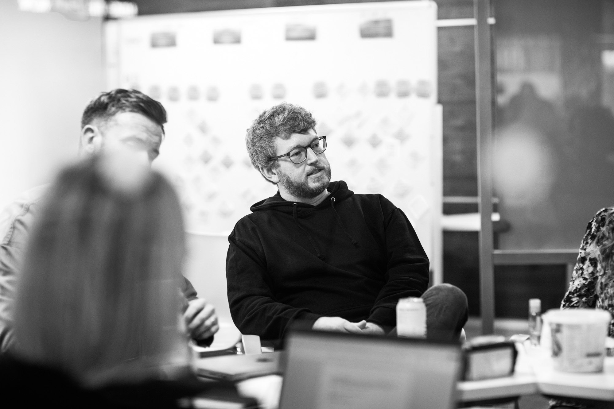 Man in glasses and black hoodie sitting at conference table during business meeting in modern office