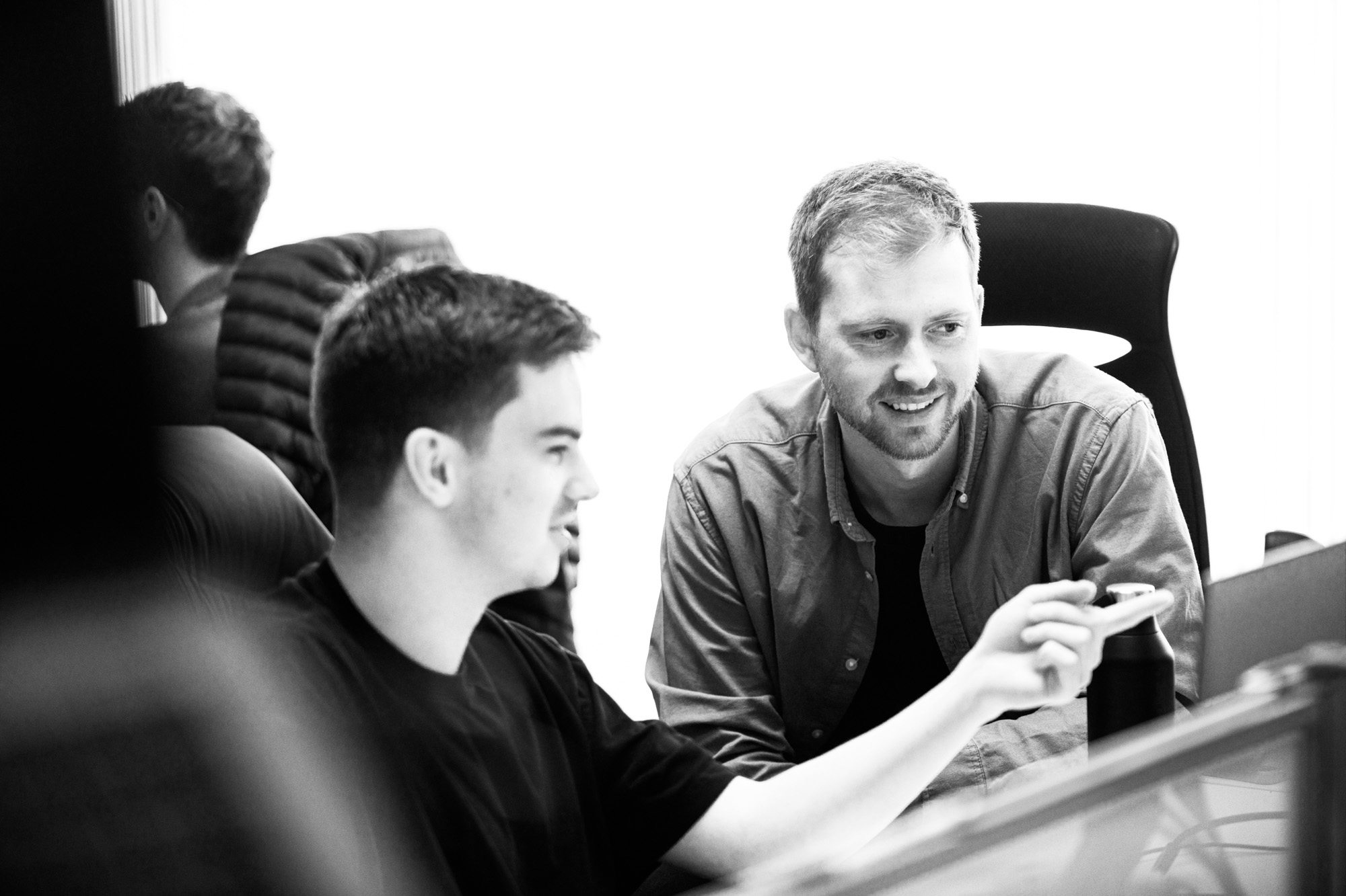 Three professionals collaborating around a computer in a bright office setting, black and white photo