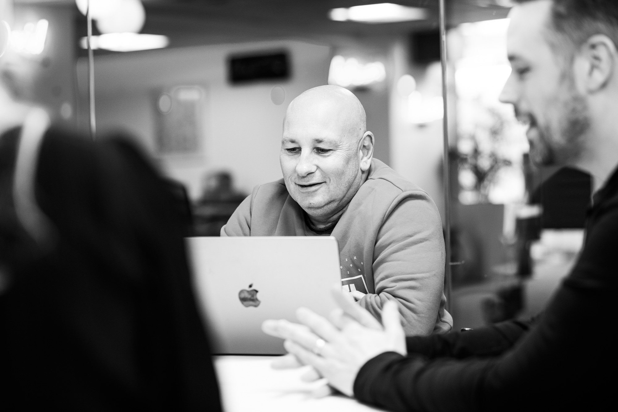 Bald man in hoodie working on laptop in modern office meeting room, black and white photo