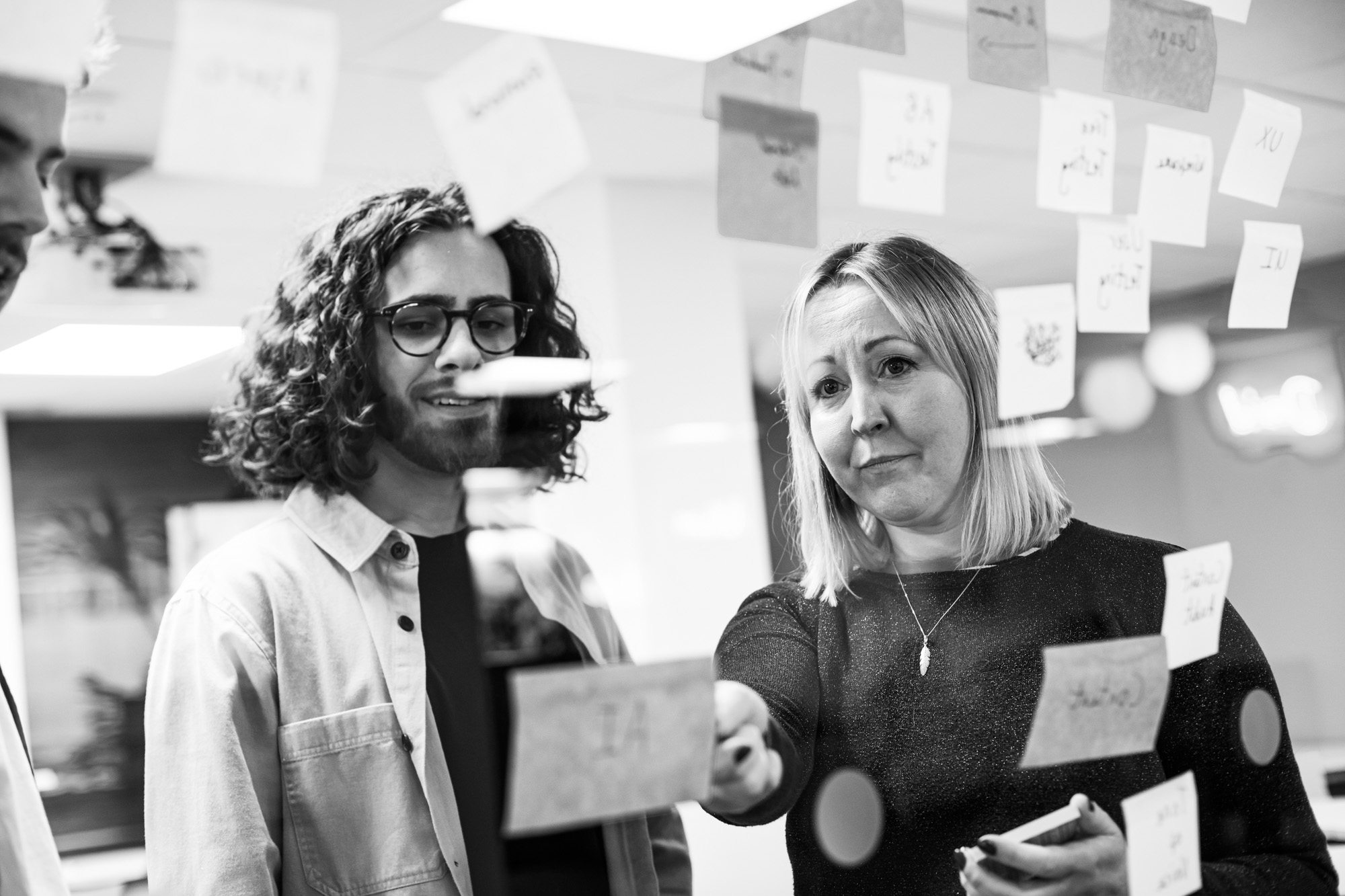 Two professionals collaborating at a glass wall covered with sticky notes in black and white