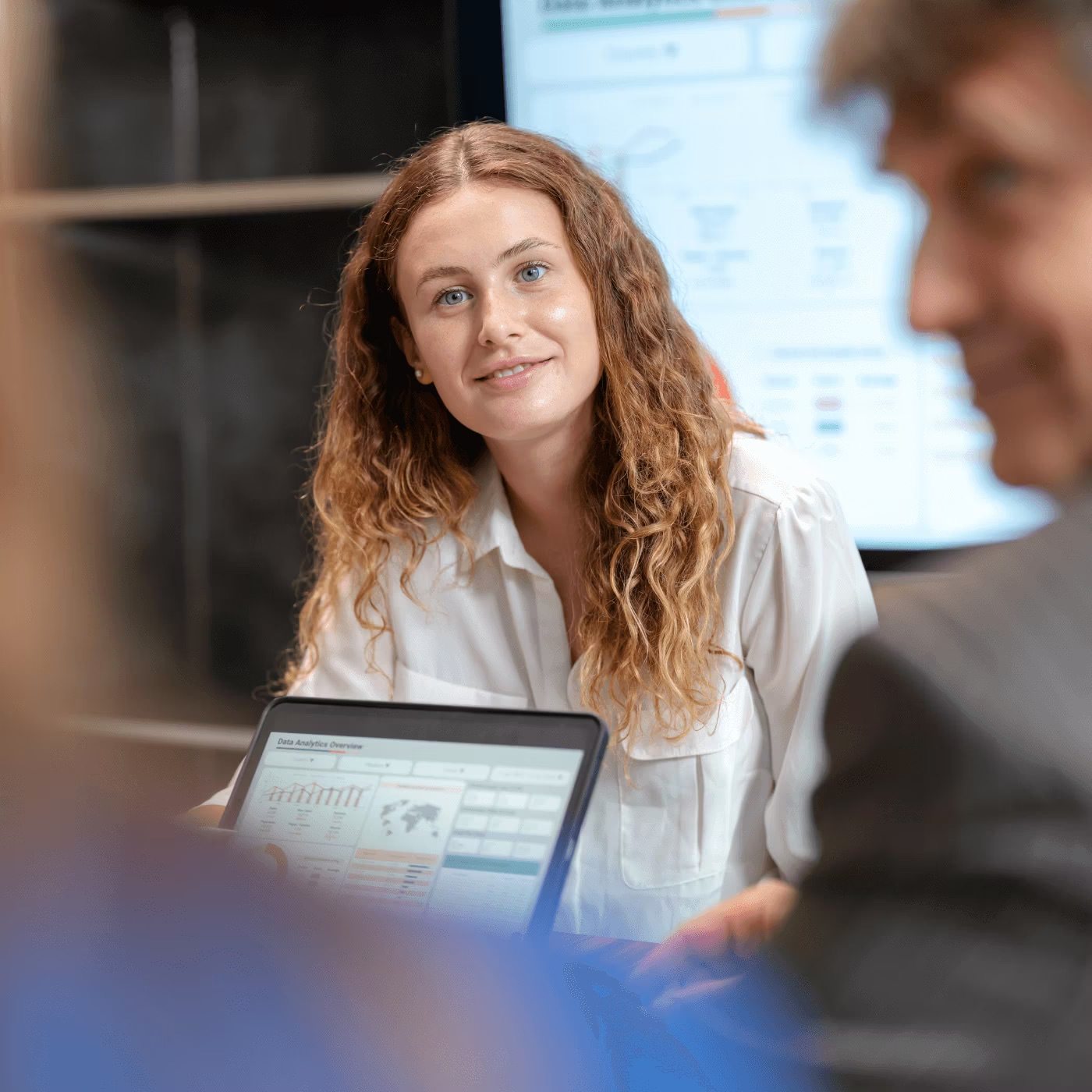 Woman with curly hair in white shirt working on laptop in modern office setting