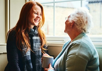 A Photo of a Young Women Talking to an Older Women who is Holding a Cup