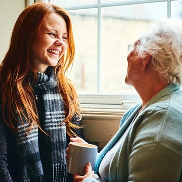 A Photo of a Young Women Talking to an Older Women who is Holding a Cup